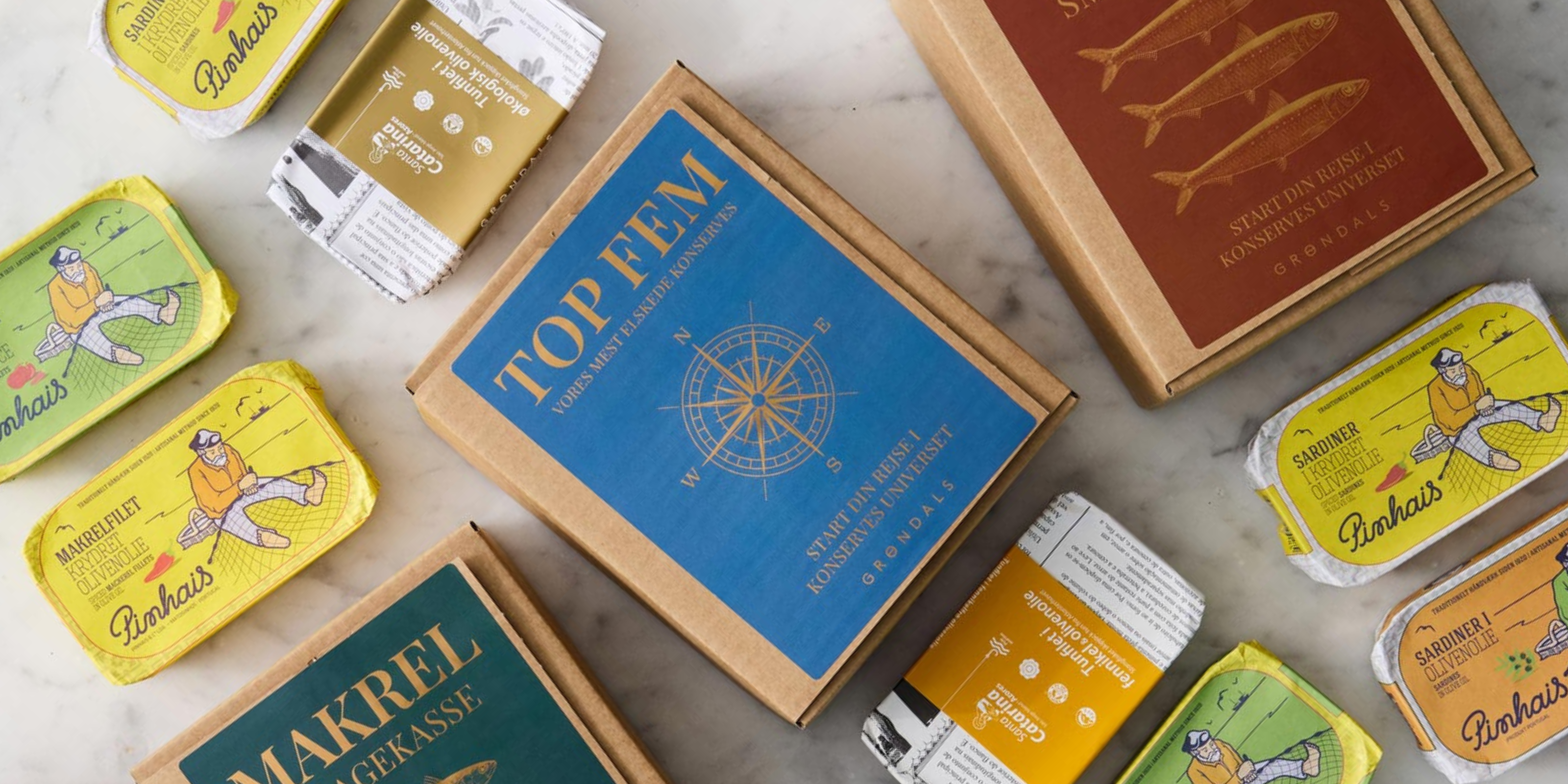 Forskellige dåser og kasser med skandinaviske fiskekonservesprodukter arrangeret på en lys marmoroverflade; emballagen har farverige illustrationer og fed tekst på svensk eller norsk.