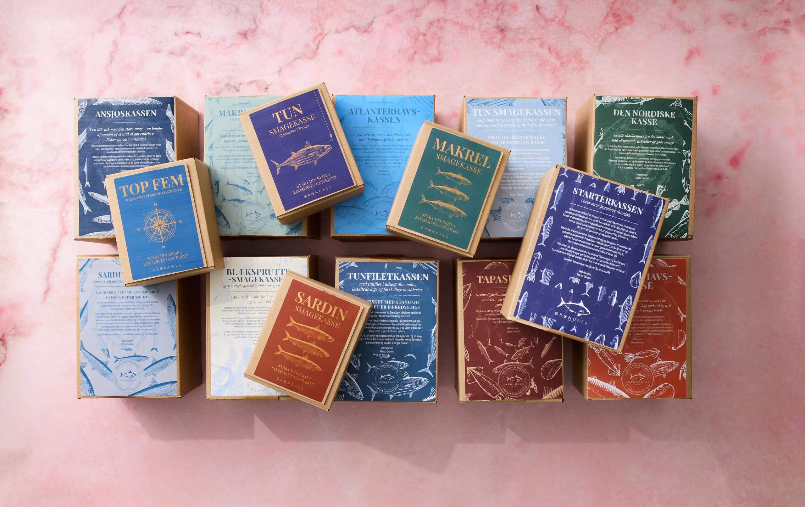 Forskellige farverige kasser med fisk og skaldyr, hver mærket med forskellige typer fisk og skaldyrssortimenter, arrangeret pænt på en lyserød marmoroverflade.