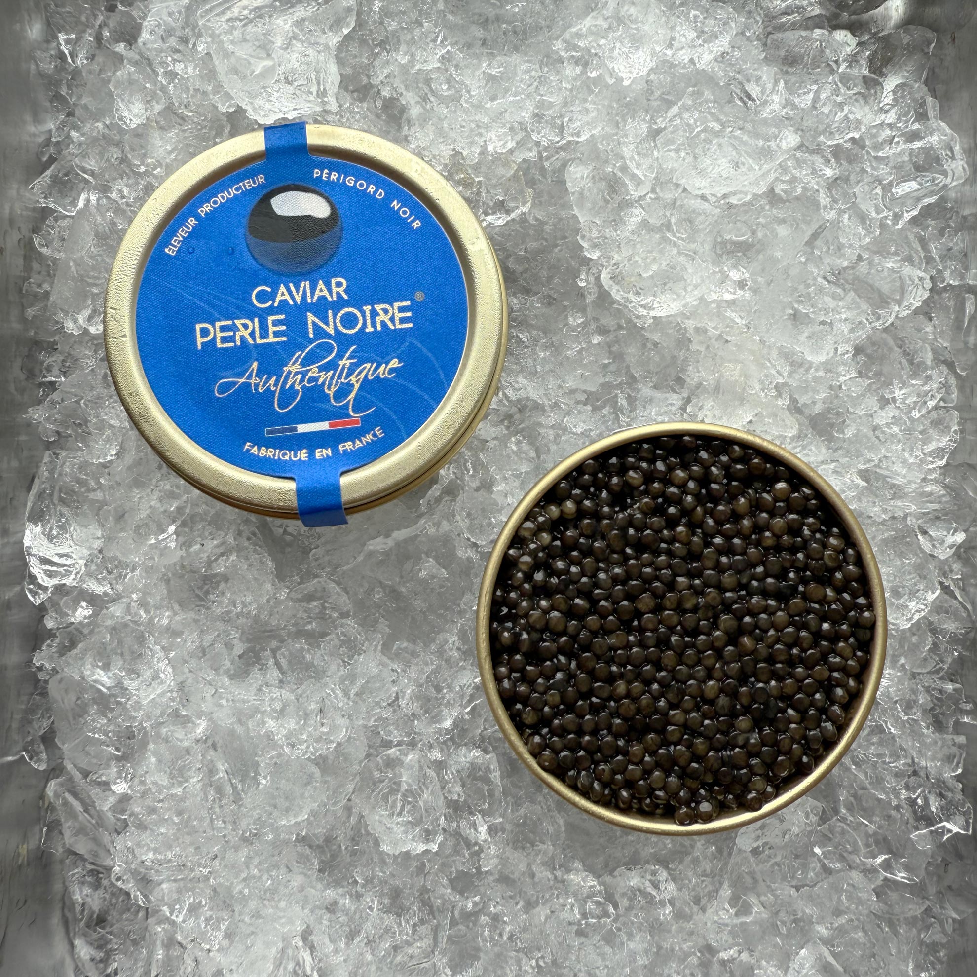 En dåse Grøndals L'Authentique (Baerii) 30g - Den klassiske kaviar, en forseglet og en åben for at afsløre autentiske kaviarperler, er elegant præsenteret på is.