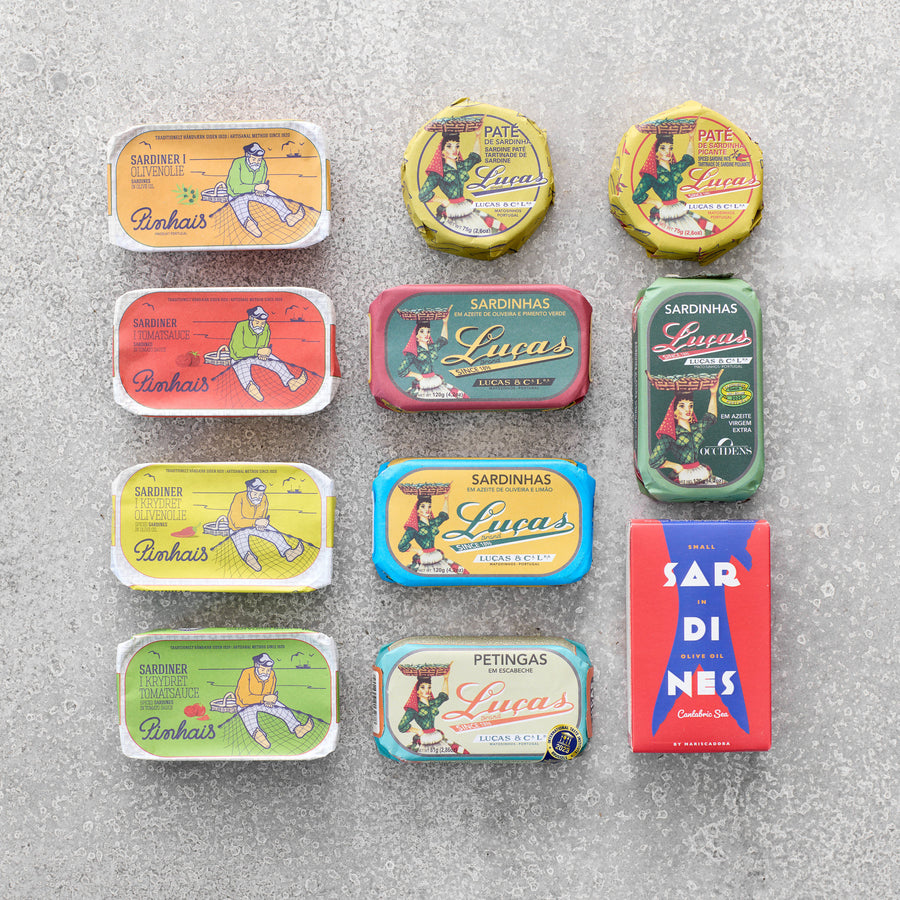 En række farverige dåser og pakker med portugisiske sardiner og paté er arrangeret pænt i et gitter på en lysegrå struktureret overflade. Hver dåse har illustrationer i vintage-stil og fede etiketter.