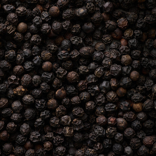 Et nærbillede af Sort Peber - i verdensklasse fra Kandy Spices viser srilankanske peberkorn med ru, teksturerede overflader og mørkebrun til sort farve, der fylder hele billedet.