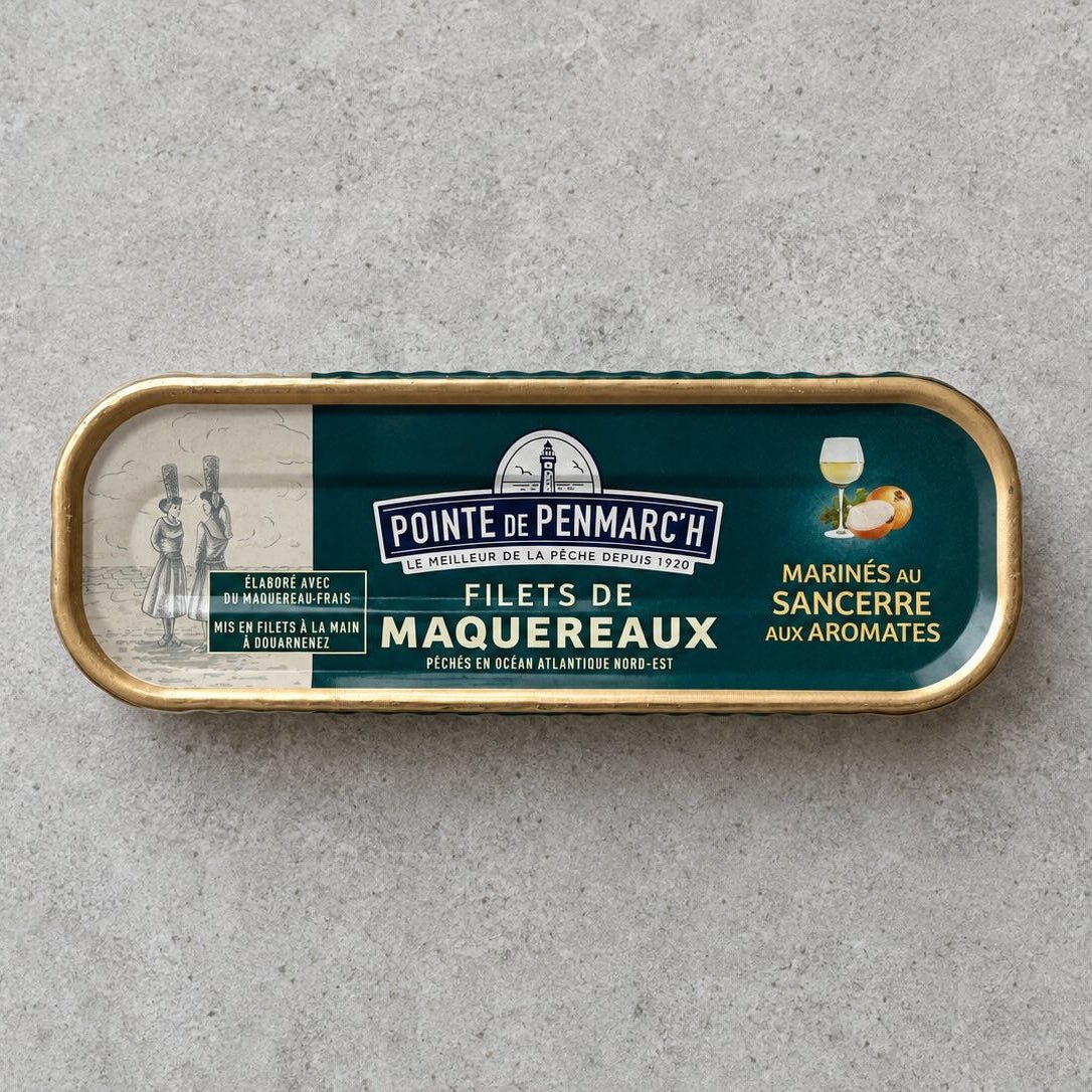 En oval dåse med Pointe de Penmarc’h Makrelfileter, marineret i Sancerre-vin og krydderurter, med en etiket, der viser to kvinder i traditionel dragt og et glas hvidvin.