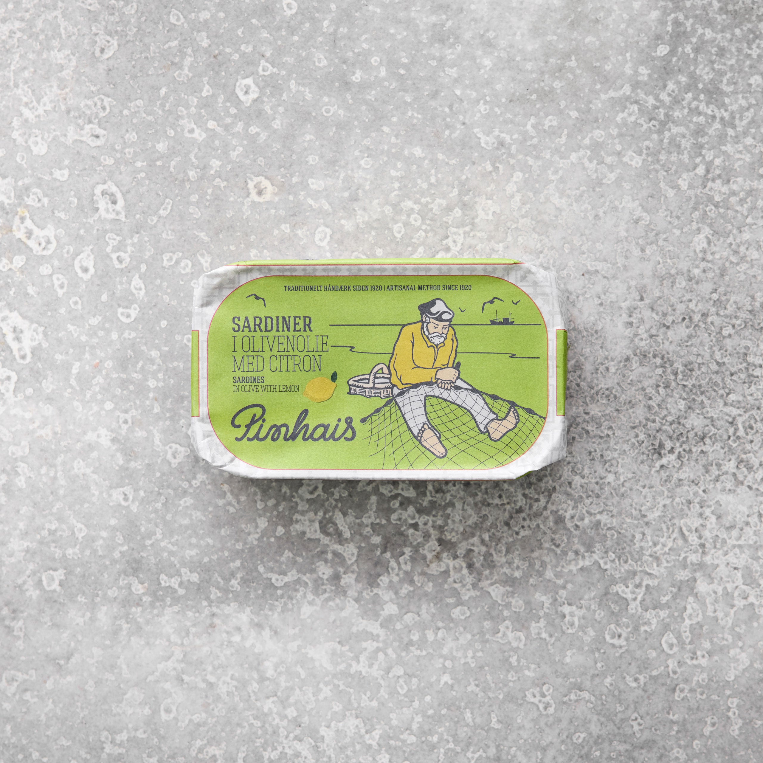 Emballage til Pinhais sardiner i olivenolie med citron fra Grøndals, med en grøn og gul illustration af en fisker, set mod en grå tekstureret baggrund.