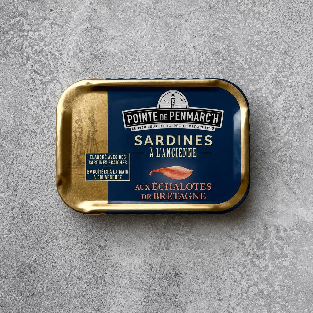 En blikdåse med guldkant med Pointe de Penmarc’h Sardiner med skalotteløg fra Bretagne, forsynet med en illustration af skalotteløg på en grå, plettet baggrund.