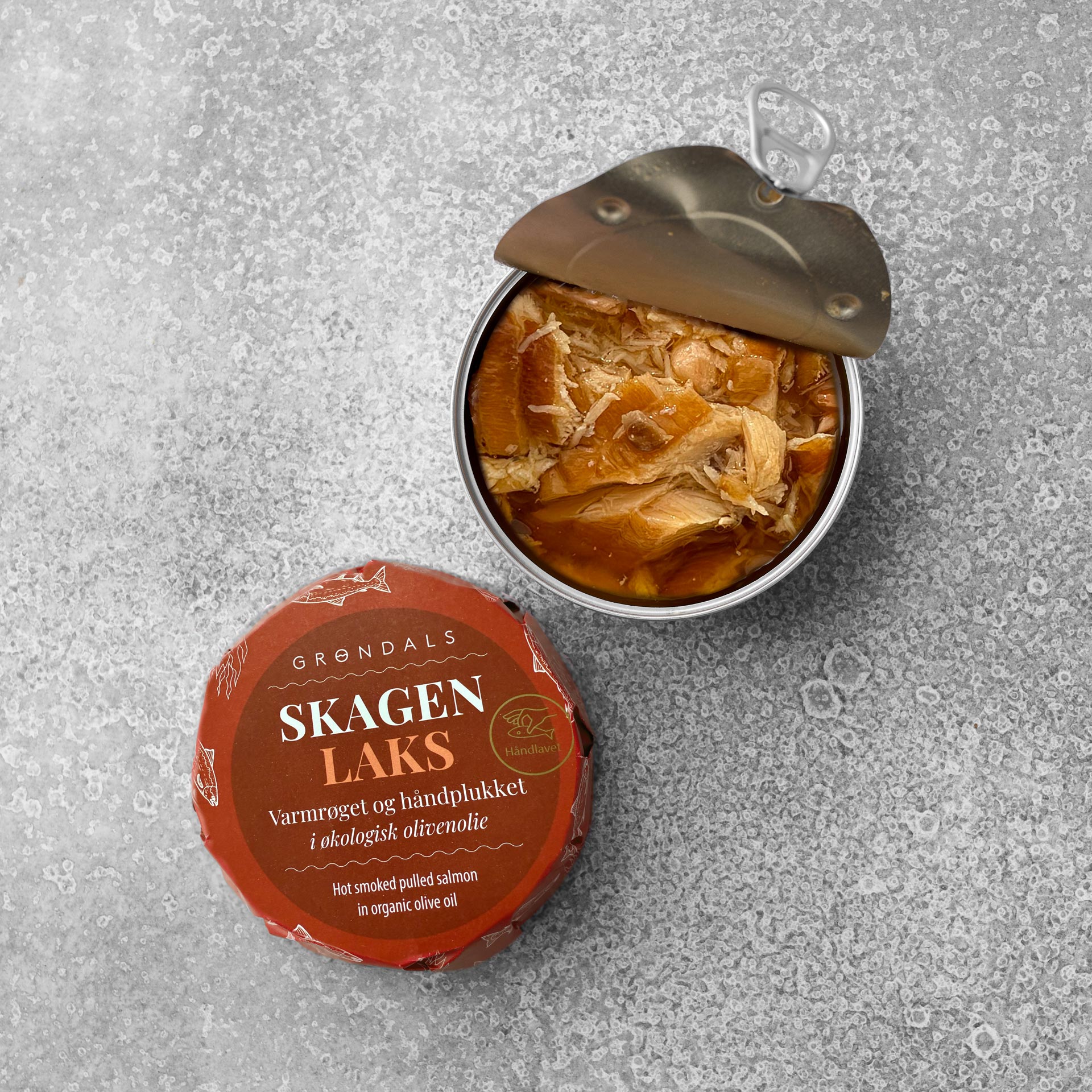En dåse Grøndals Varmrøget håndplukket laks i økologisk olivenolie står på en grå, struktureret overflade, åbnet for at afsløre laksestykker og med det røde låg, der viser Grøndals-mærket ved siden af.