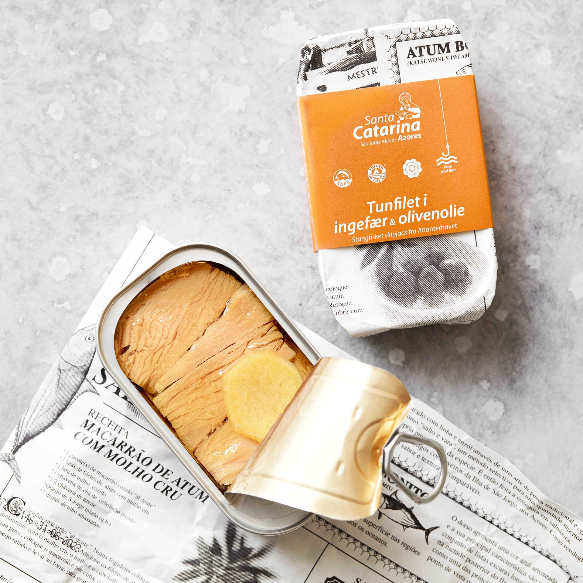 En åbnet dåse Santa Catarina Tunfilet i ingefær og olivenolie hviler på papir, med sin orange og hvide emballage – mærket BPA-fri dåser – synlig ved siden af.