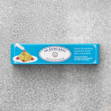 En blå rektangulær æske med Olasagasti Ansjospuré med olivenolie (60 g) ligger på en struktureret grå overflade og viser pasta med velsmagende ansjoscreme, tomater og flersproget information om bæredygtige ansjoser.