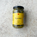 En glaskrukke med Spanske delikatesse cornichoner fra Don Gastronom med en gul etiket og sort låg er præsenteret på en lys, tekstureret overflade; perfekt til servering til tapas.