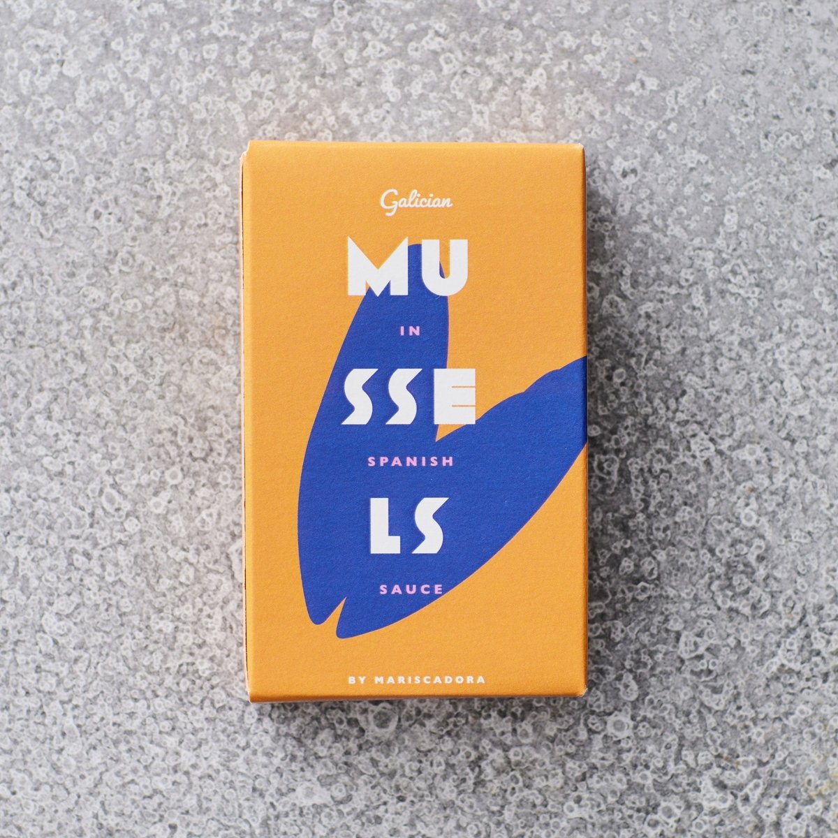 En rektangulær orange æske mærket "Friterede muslinger i escabeche" af Don Gastronom med fed hvid og blå tekst, abstrakte blå skaldesigns og ordet "escabeche" vises på en struktureret grå overflade.