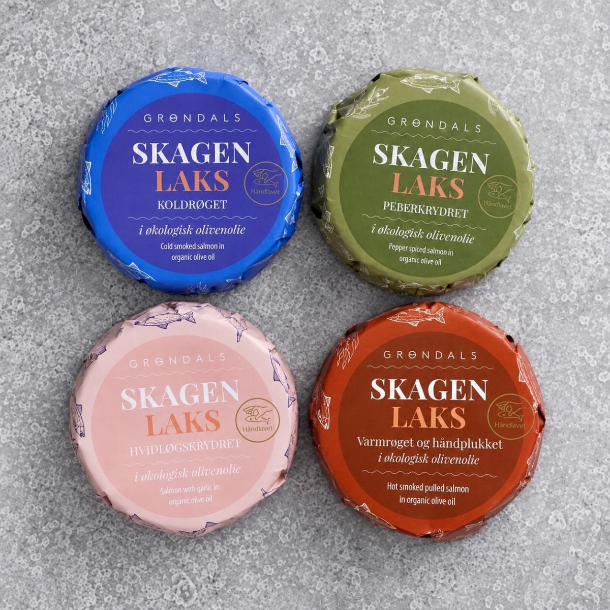 Fire runde pakker med Grøndals’ lakse-kvartet, indpakket i blåt, grønt, lyserødt og orange af Grøndals, er anbragt i en firkant på en grå overflade med struktur.