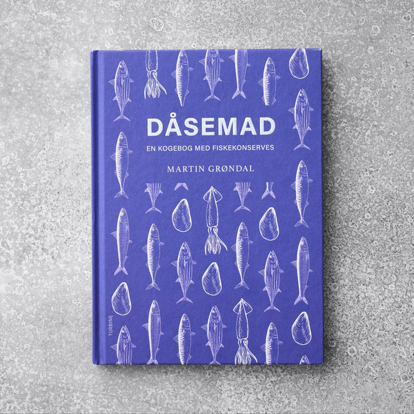 Den lilla kogebog "Kogebogen DÅSEMAD" fra Grøndals viser illustrationer af hvid fisk og skaldyr på omslaget, hvilende på en tekstureret grå overflade.
