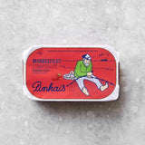 En rektangulær dåse med Pinhais Makrelfilet i tomatsauce har en rød etiket med en illustration af en fisker, der sidder på et net, og en båd i baggrunden.