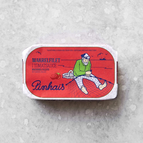 En rektangulær dåse med Pinhais Makrelfilet i tomatsauce har en rød etiket med en illustration af en fisker, der sidder på et net, og en båd i baggrunden.