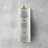 En 500 ml metalbeholder med KAVALARIA ESTATE Økologisk Ekstra Jomfru Olivenolie står oprejst på en struktureret grå overflade og er prydet med et minimalistisk logo i hvidt og guld samt en lille illustration af en bygning fra Kreta.