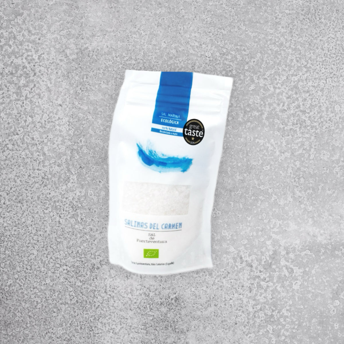 En hvid og blå pose med »Sal de Fuerteventura Økologisk Havsalt – Håndhøstet fra Fuerteventura« står på en lysegrå, struktureret overflade med et sort »Great Taste«-mærke og blå logooplysninger øverst.