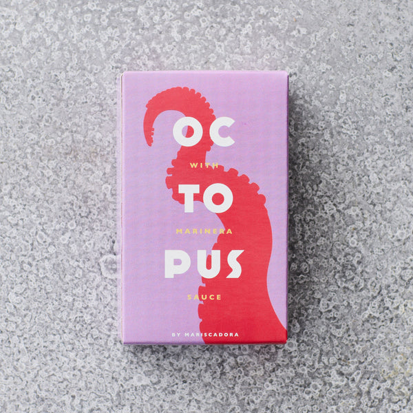 En rektangulær æske med et lilla og pink design med en rød blækspruttearm. Teksten på æsken lyder: OCTOPUS with marinera sauce by Mariscadora, på en spættet grå overflade.