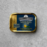 En rektangulær dåse med Pointe de Penmarc’h Sardiner i ekstra jomfruolivenolie med en marineblå etiket, der viser en illustration af en citron og to personer i traditionel bretonsk dragt.