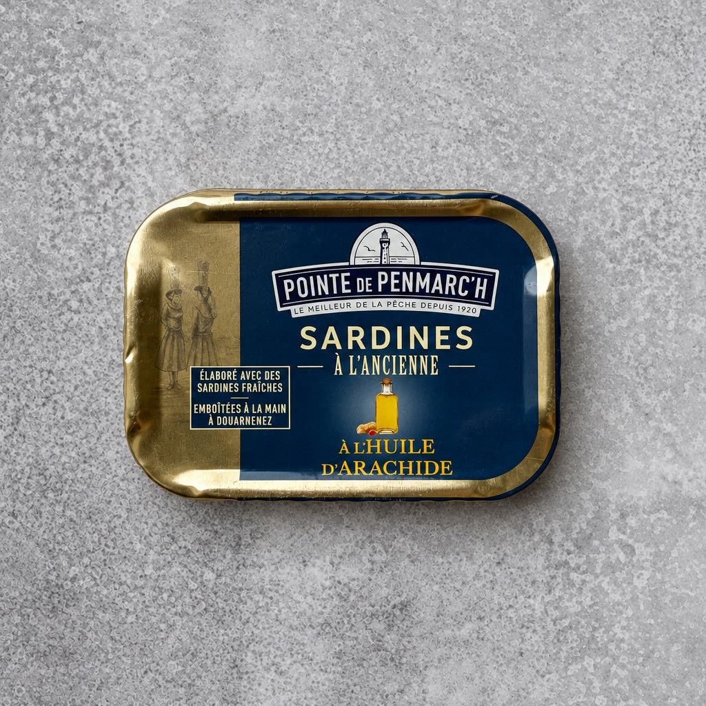 Rektangulær dåse med Pointe de Penmarc’h Sardiner i jordnøddeolie med en marineblå etiket, der viser en illustration af et fyrtårn.