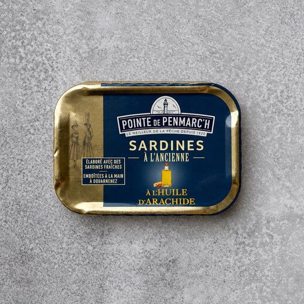 Rektangulær dåse med Pointe de Penmarc’h Sardiner i jordnøddeolie med en marineblå etiket, der viser en illustration af et fyrtårn.