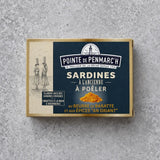 Rektangulær dåse med Pointe de Penmarc’h Sardiner med kærnet smør og karrykrydderier med en marineblå etiket, der viser kvinder med kurve, et fyrtårnslogo og en bunke gult karrypulver.