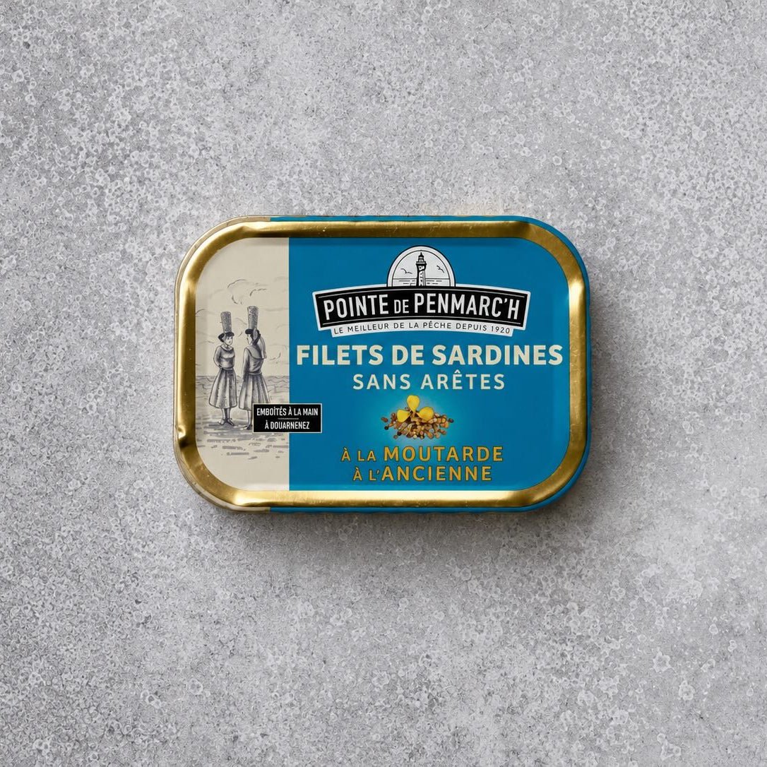 Rektangulær dåse med Pointe de Penmarc’h Sardinfileter med gammeldags sennep med en blå etiket, der viser et fyrtårn og en illustration af to personer.
