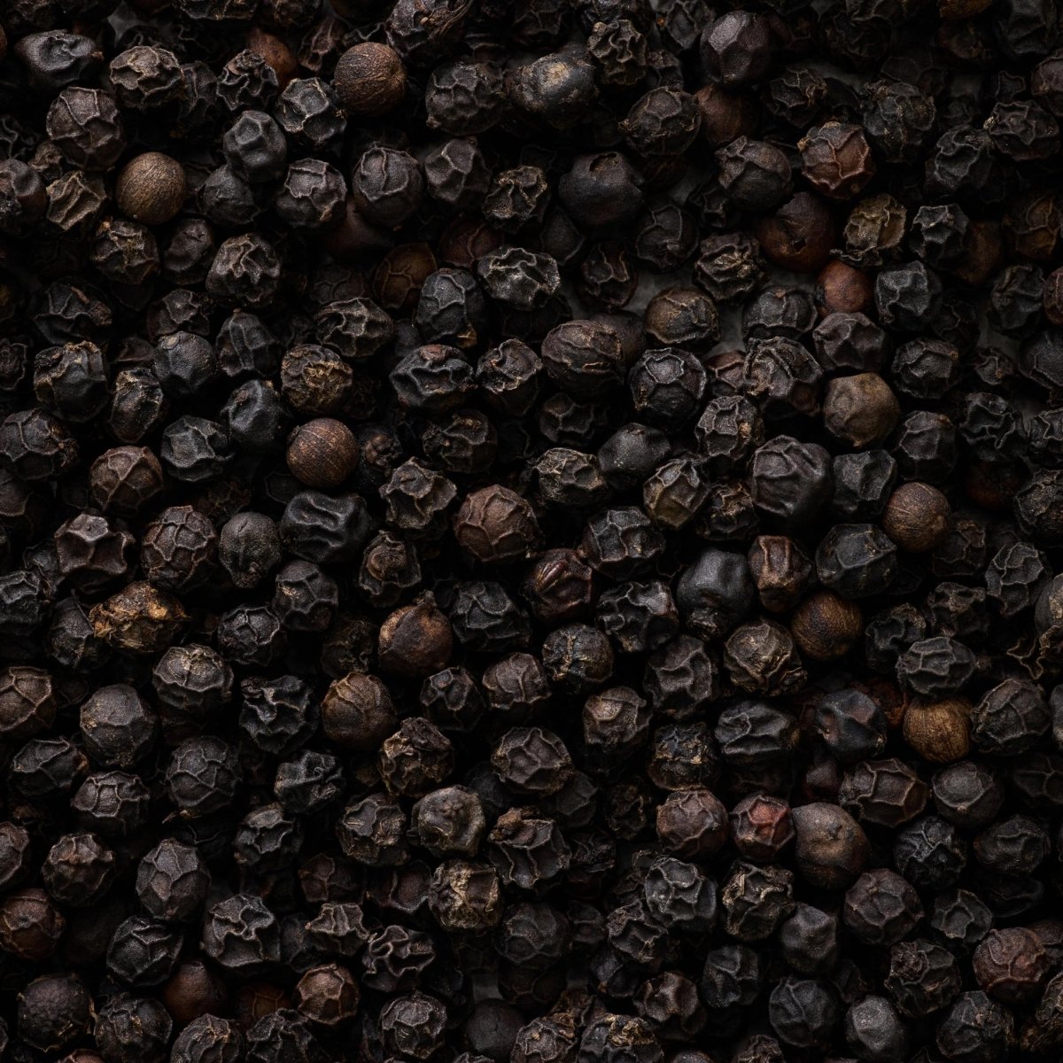 Et nærbillede af Sort Peber - i verdensklasse fra Kandy Spices viser srilankanske peberkorn med ru, teksturerede overflader og mørkebrun til sort farve, der fylder hele billedet.