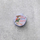 En lille rund dåse Lucas Spicy tunpaté med en vintage-etiket, der viser en kvinde, der bærer en kurv på hovedet, placeret på en tekstureret grå overflade.