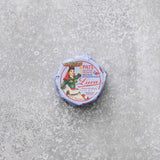 En lille rund dåse Lucas Spicy tunpaté med en vintage-etiket, der viser en kvinde, der bærer en kurv på hovedet, placeret på en tekstureret grå overflade.