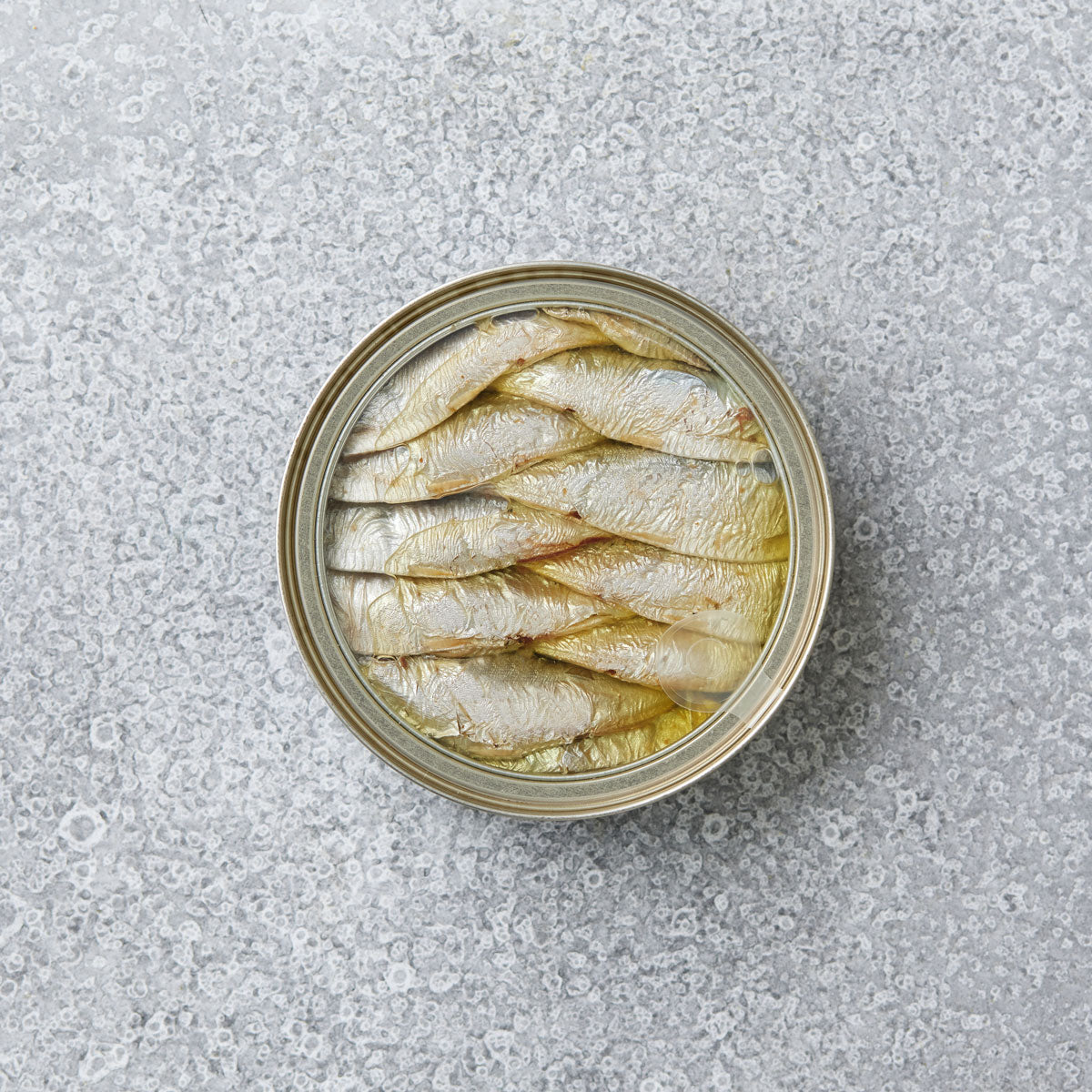 En åben dåse Riga Gold Små brislinger i olivenolie står på en lysegrå, spættet overflade – en sand delikatesse.