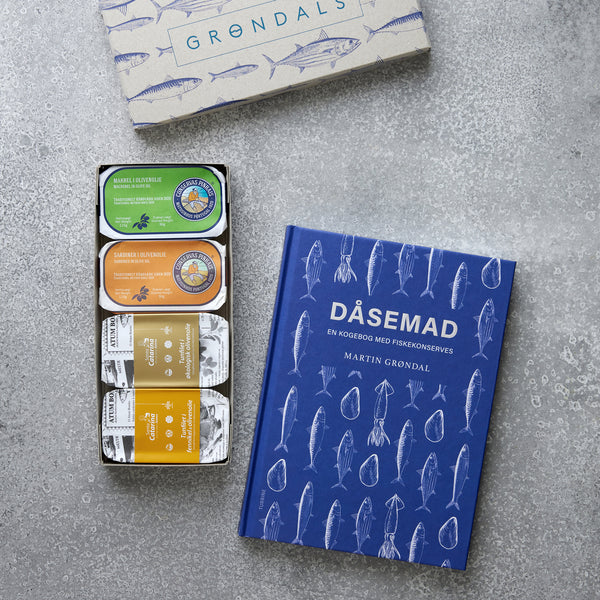 Grøndals' Værtsgave og DÅSEMAD inkluderer en blå fiske-illustreret kogebog og fire farverige fiskekonserves i mærkevareemballage - et perfekt Grøndals-gavesæt udstillet på en grå overflade.