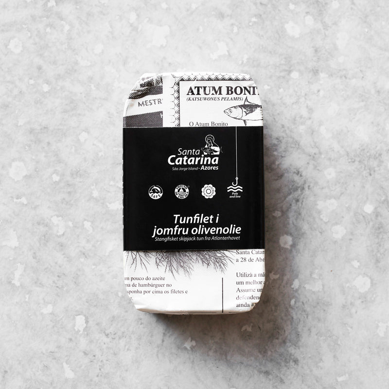 En rektangulær dåse Santa Catarina Tunfilet i jomfru olivenolie hviler på en spættet grå overflade. Den sort-hvide emballage har dansk og portugisisk tekst med vægt på den bæredygtige fangstmetode.