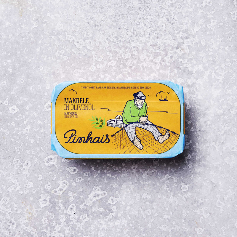 En gul og blå dåse Pinhais Små makroller i olivenolie, en portugisisk delikatesse, viser en fisker, der reparerer et net med både og fugle i baggrunden, placeret på en lys, tekstureret overflade.